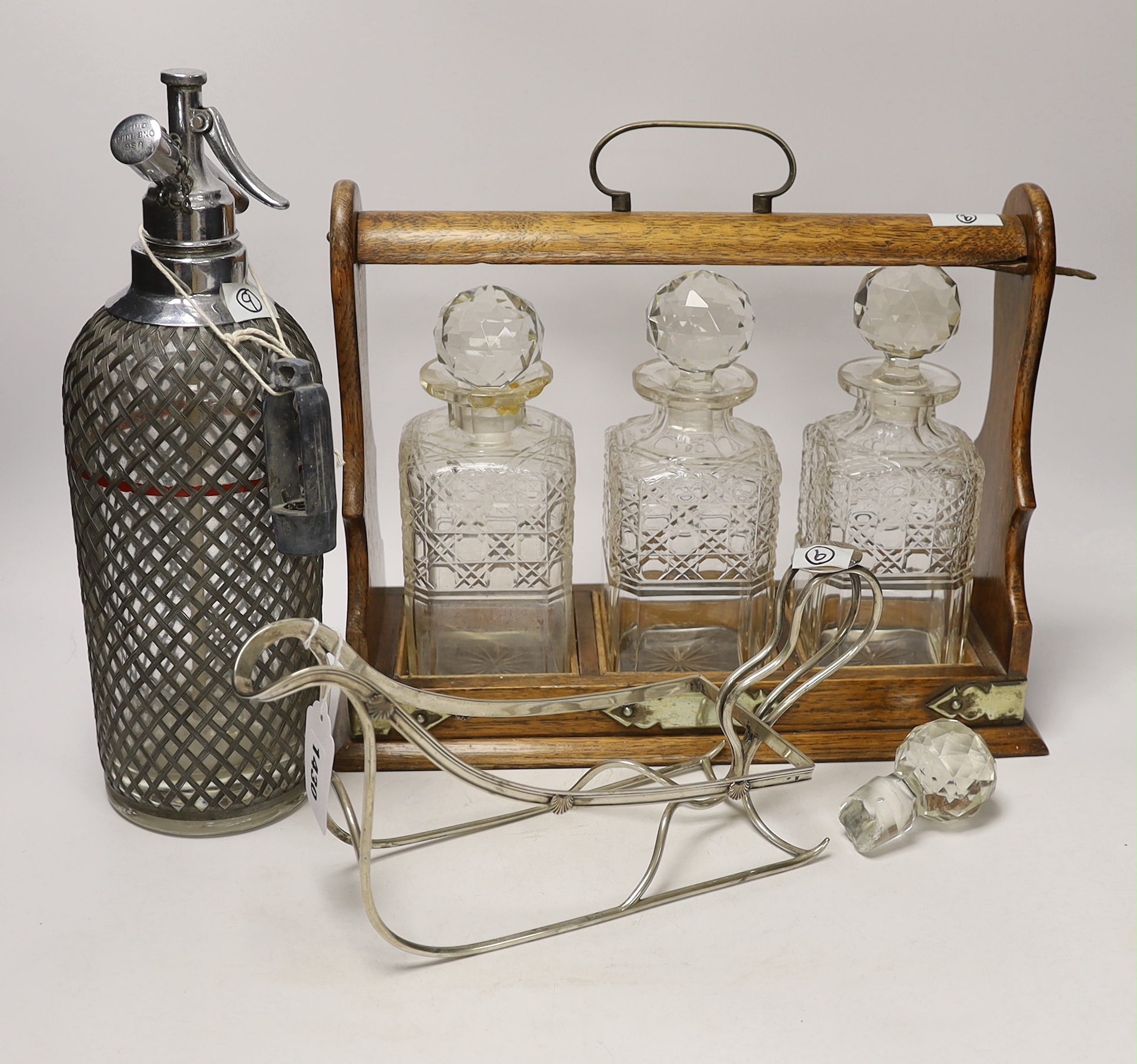 An oak three bottle tantalus, a German 800 standard white metal bottle cage and a vintage soda syphon, 36cm wide